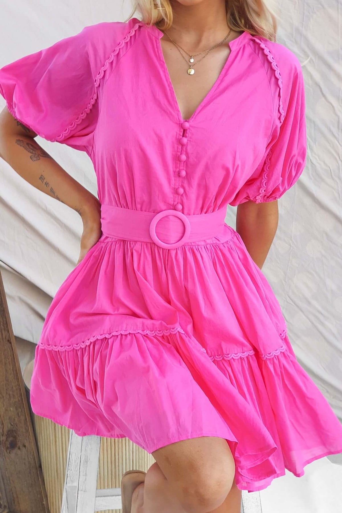 Model wearing a pink Verlaine dress featuring a V-neckline, button-up bust, and a removable tie.