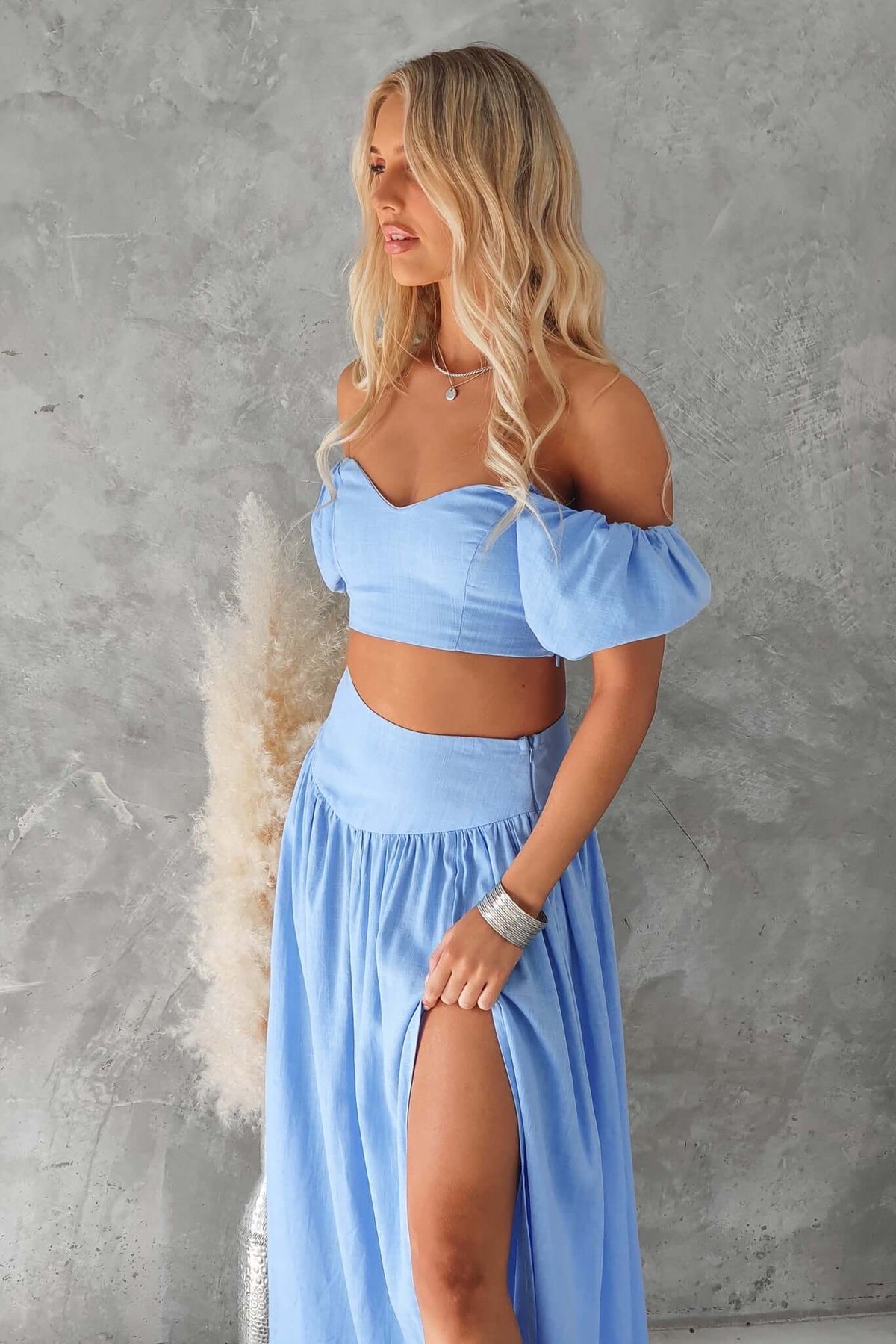 Model wearing a light blue off-shoulder crop top and matching skirt, showcasing a stylish summer look.