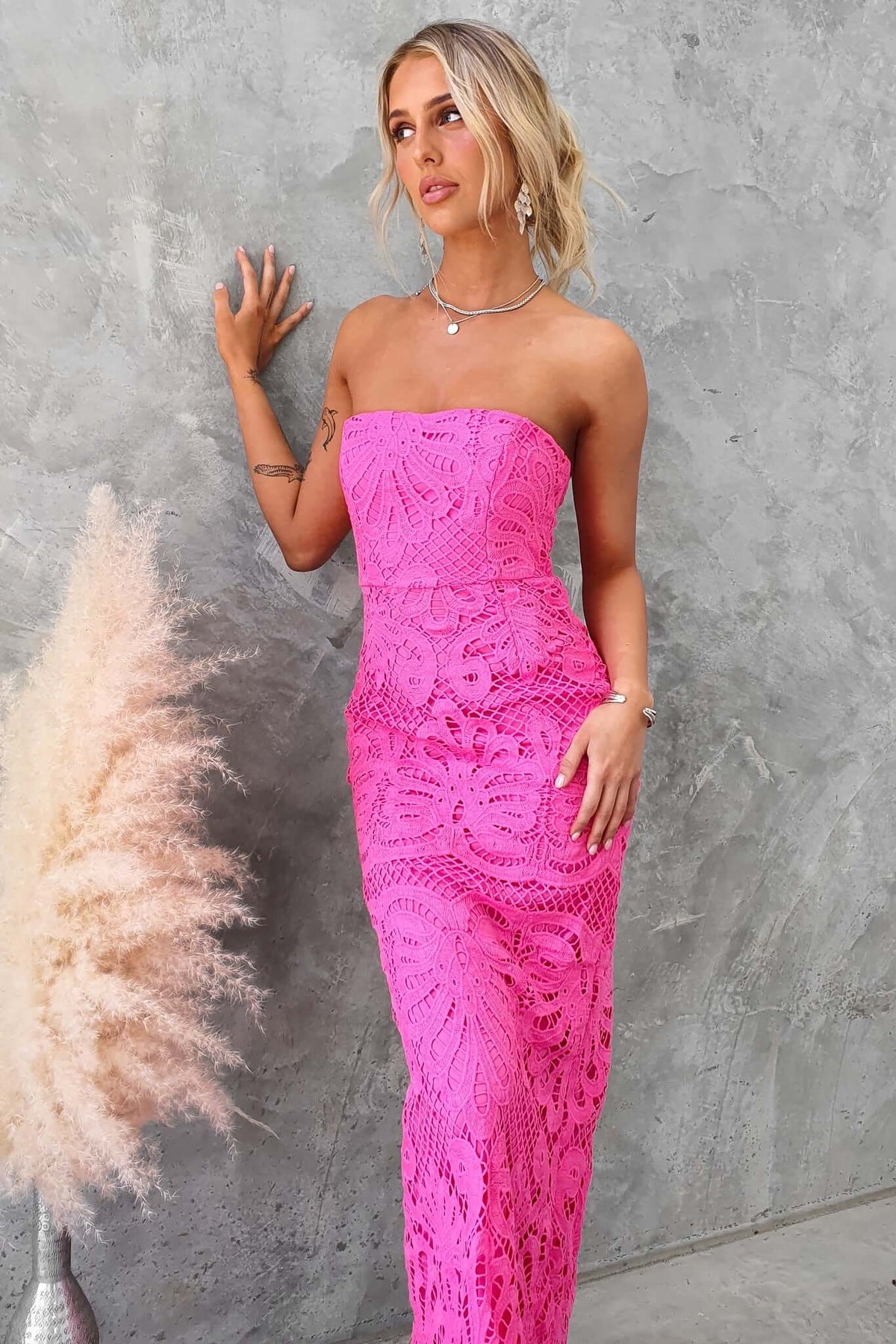 Model wearing a strapless pink maxi dress with lace material, featuring an elegant design and a back split.