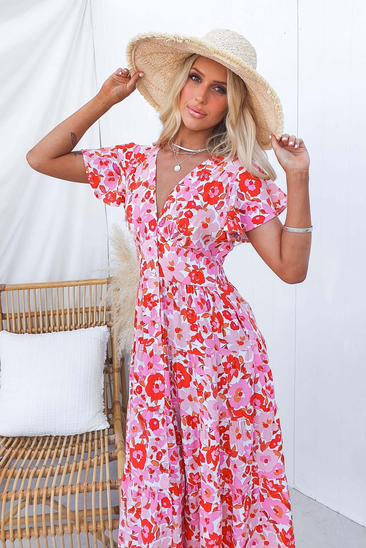 Blonde woman wearing a floral midi dress and straw hat, posing elegantly in a bright, airy setting.
