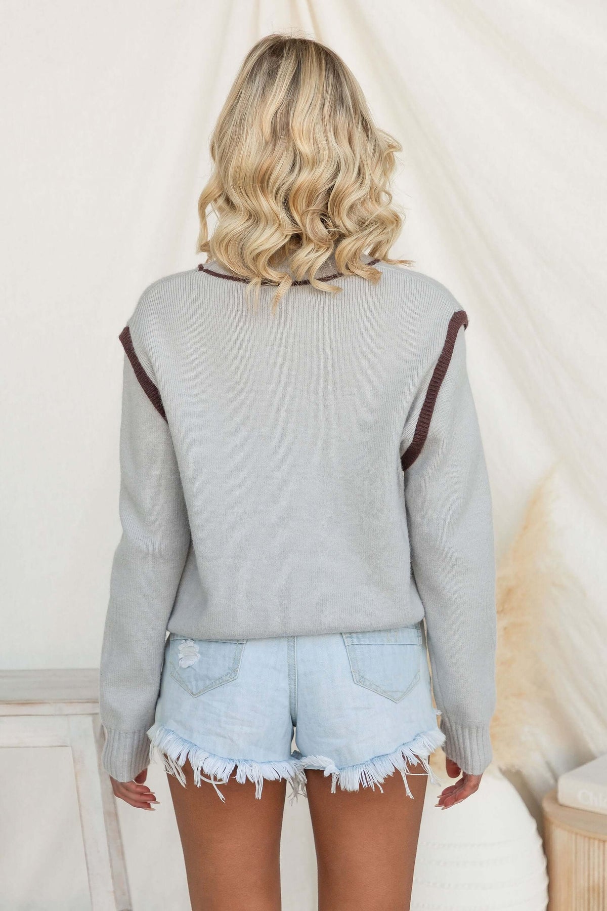 Back view of a woman wearing a Nights Out Jumper with mock neckline and knit material, paired with denim shorts.