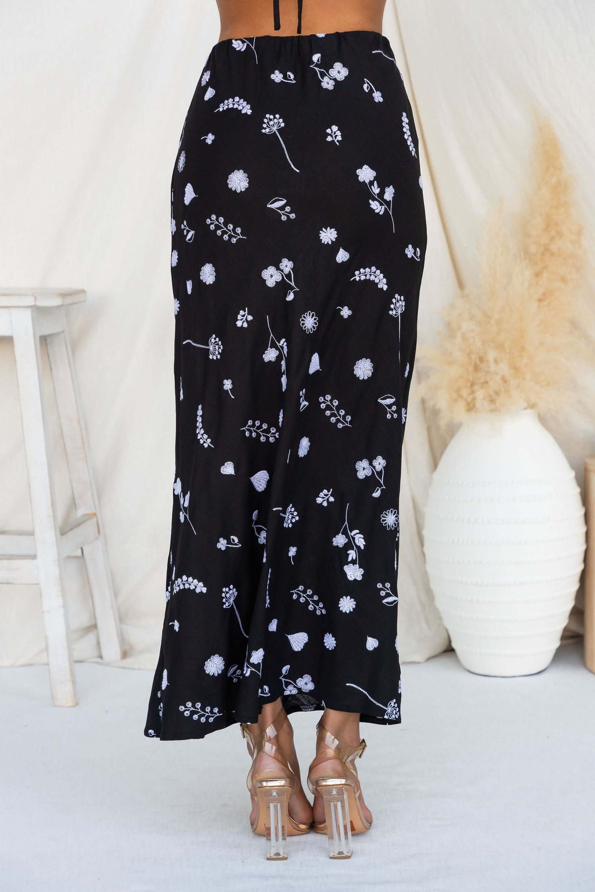 Lune Maxi Skirt featuring a black fabric with floral embroidery, styled with clear heeled sandals.