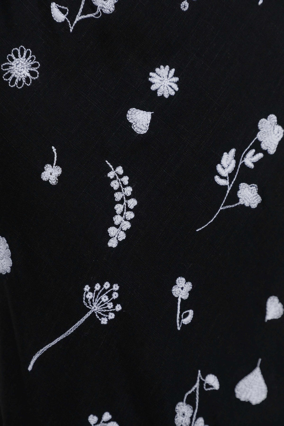Lune Top black fabric with intricate white floral embroidery design, showcasing detailed patterns.