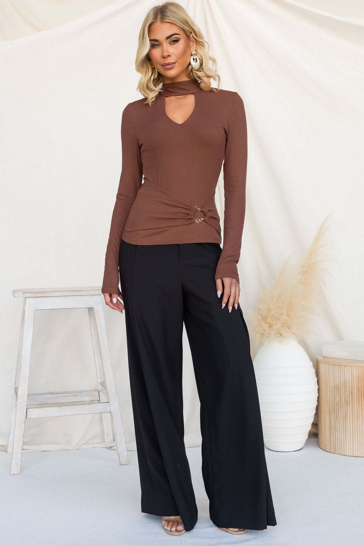 Model wearing Manor Top in brown with high neckline, ribbed detail, and gold hardware.