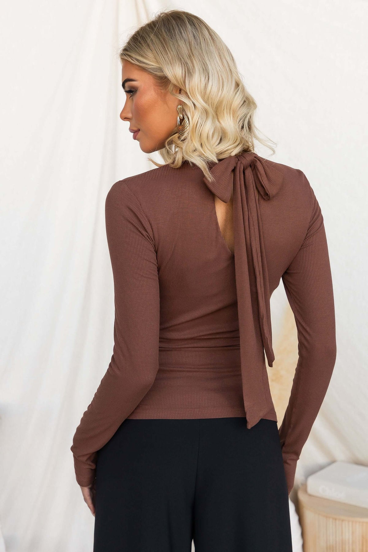 Back view of a woman wearing the Manor Top with a high neckline and tie detail, showing ribbed texture.