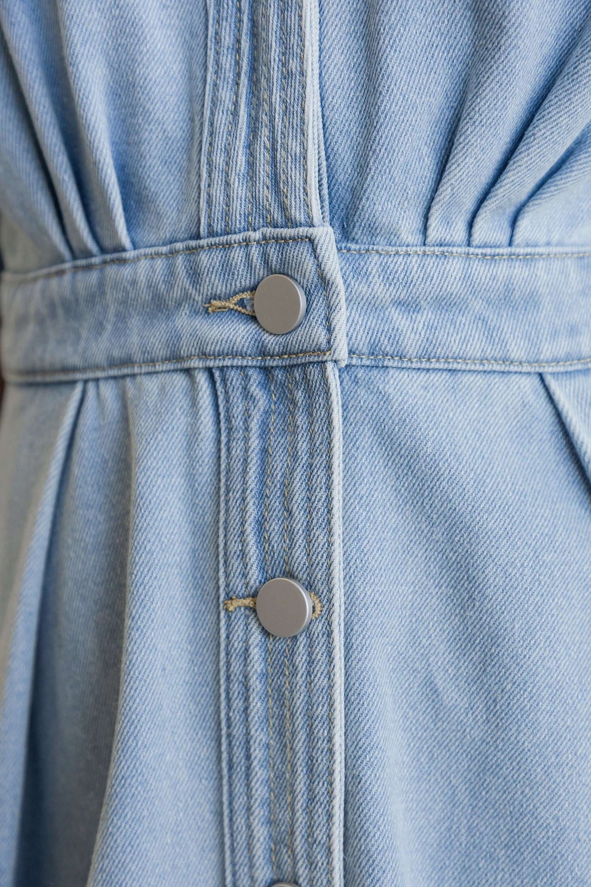 Close-up of buttons and fabric on Saddle Bloom Denim Midi Dress, featuring a light blue wash and denim texture.