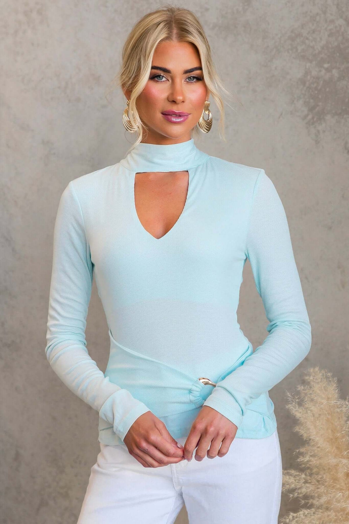 Model wearing the Manor Top in light blue with high neckline and tie detail, featuring ribbed material and gold hardware.