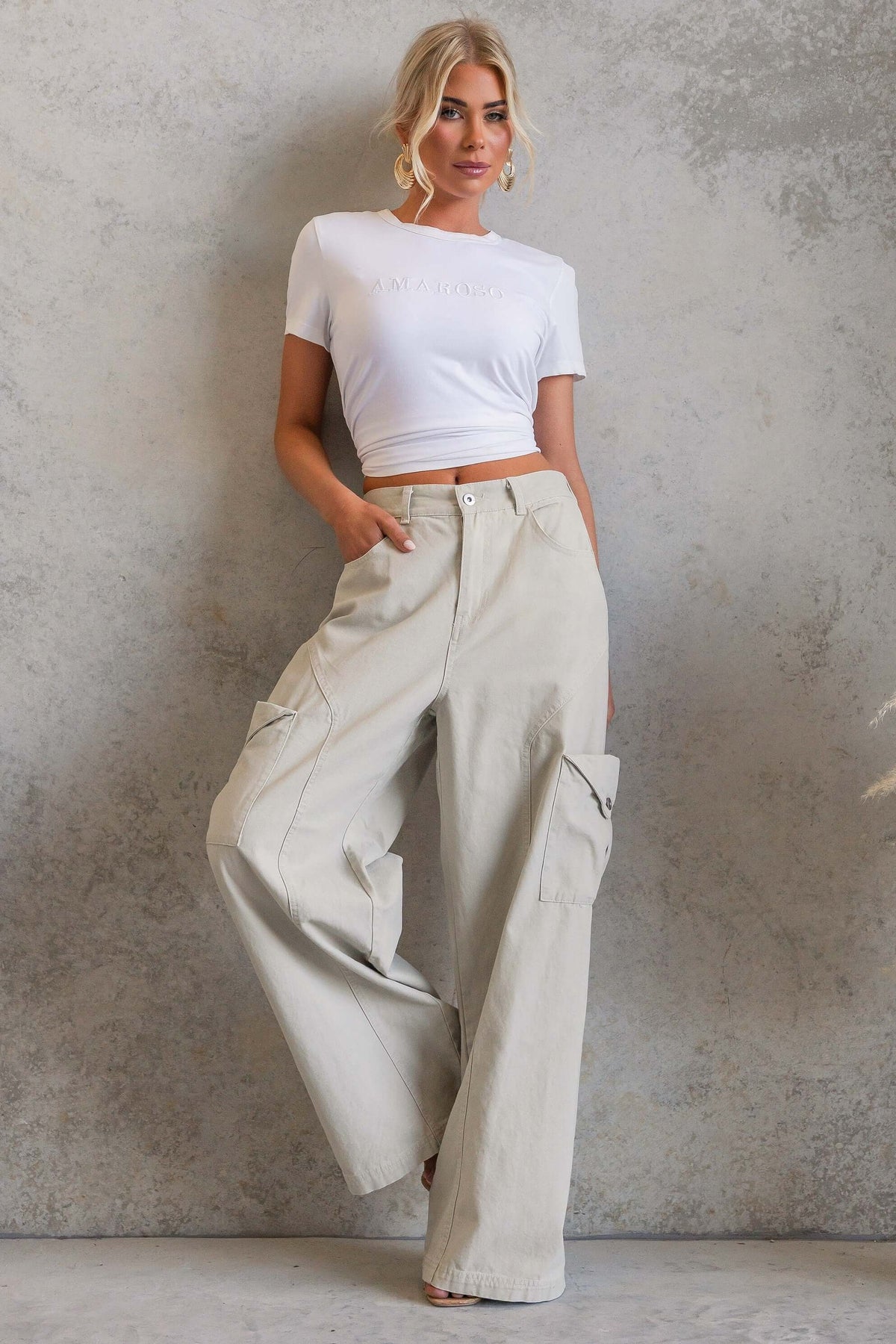 Model wearing Rebel Cargo Jeans with a cropped white top against a textured background.