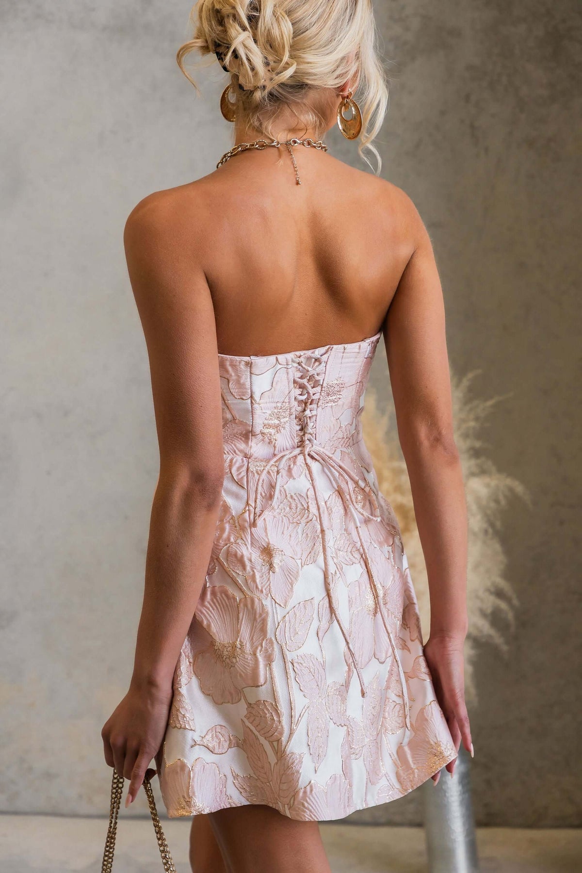 Back view of a model wearing a strapless Matilda Dress with lace-up style and textured metallic material.