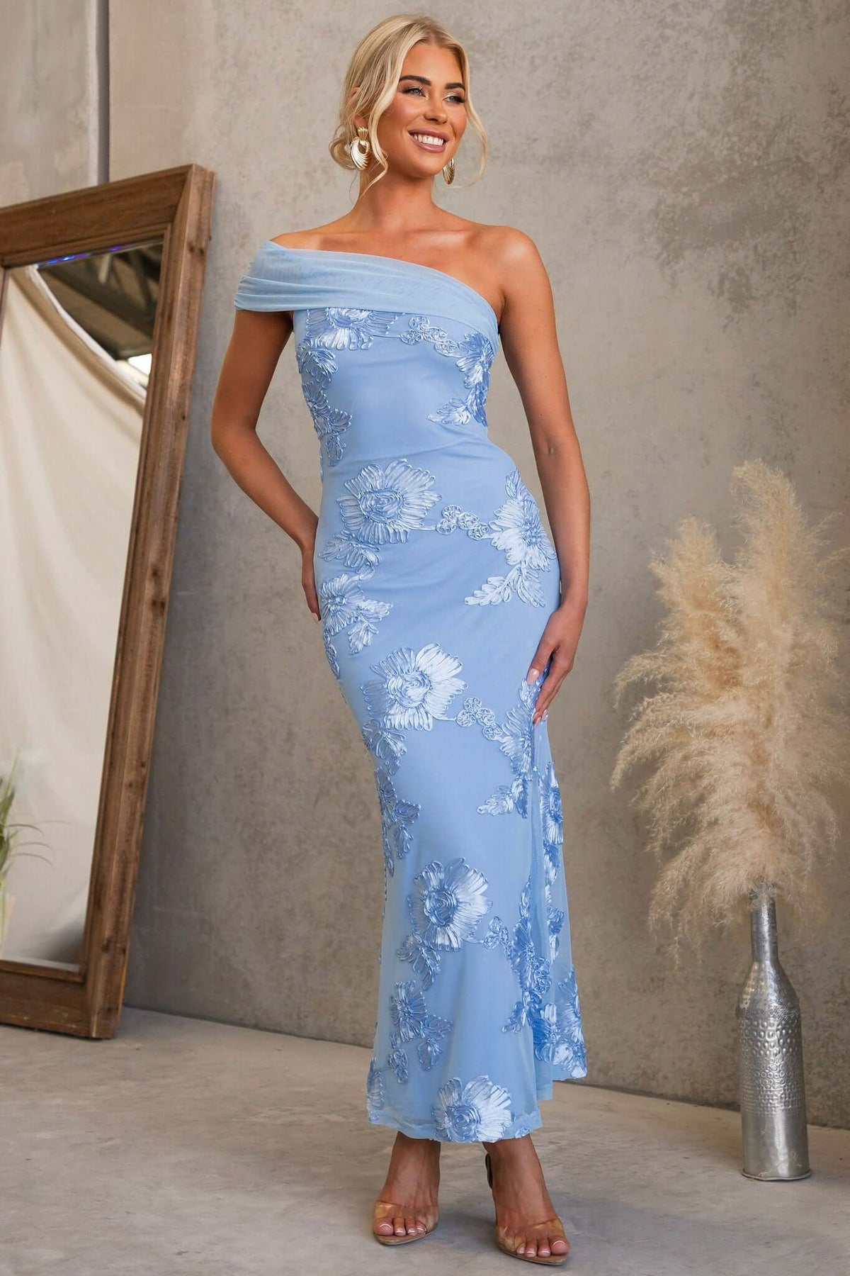 Model wearing the Korren Maxi Dress in blue with floral embroidery and a one-shoulder neckline.