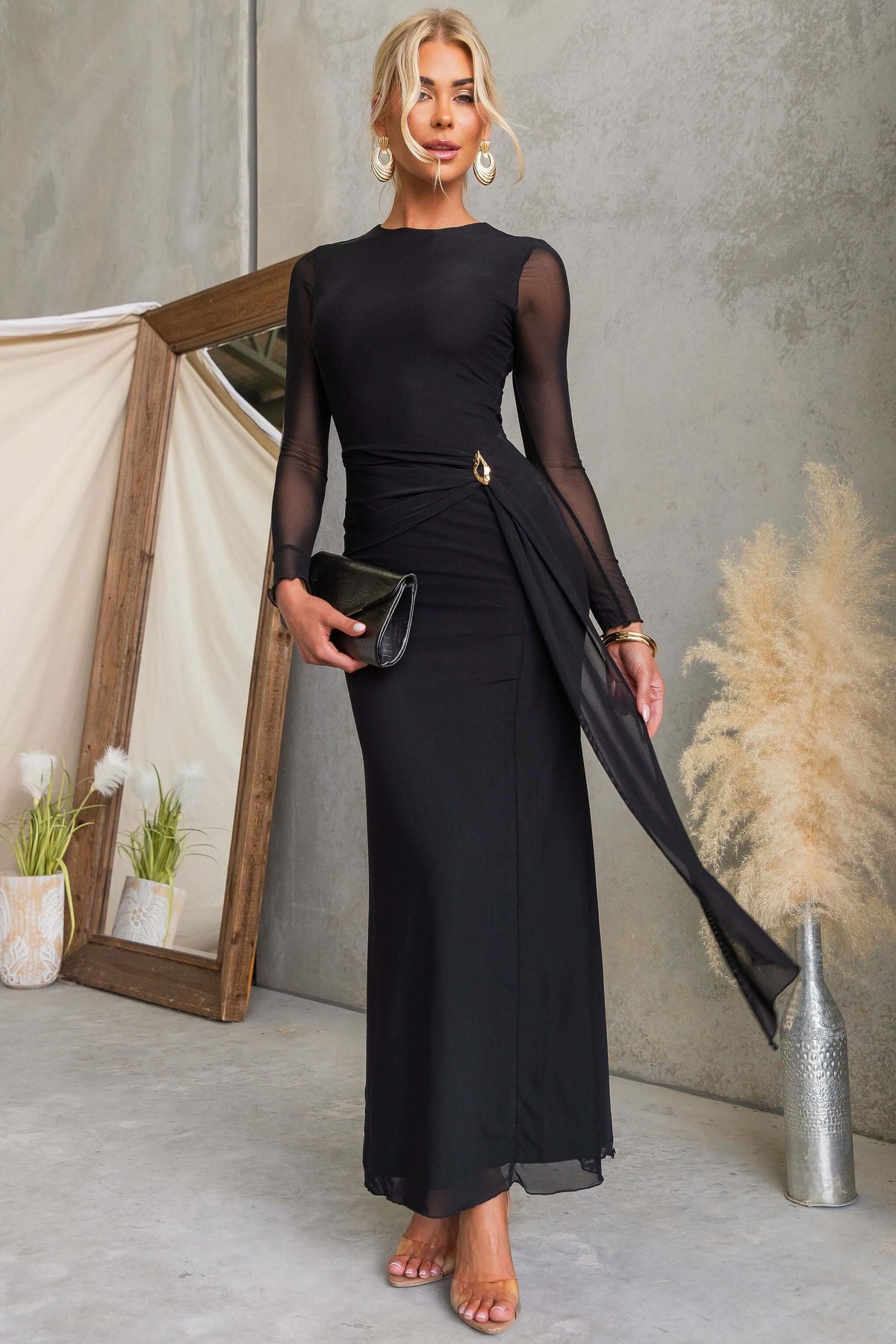 Model wearing La Rose Maxi Dress, featuring black draping material, round neckline, and chic gold hardware.
