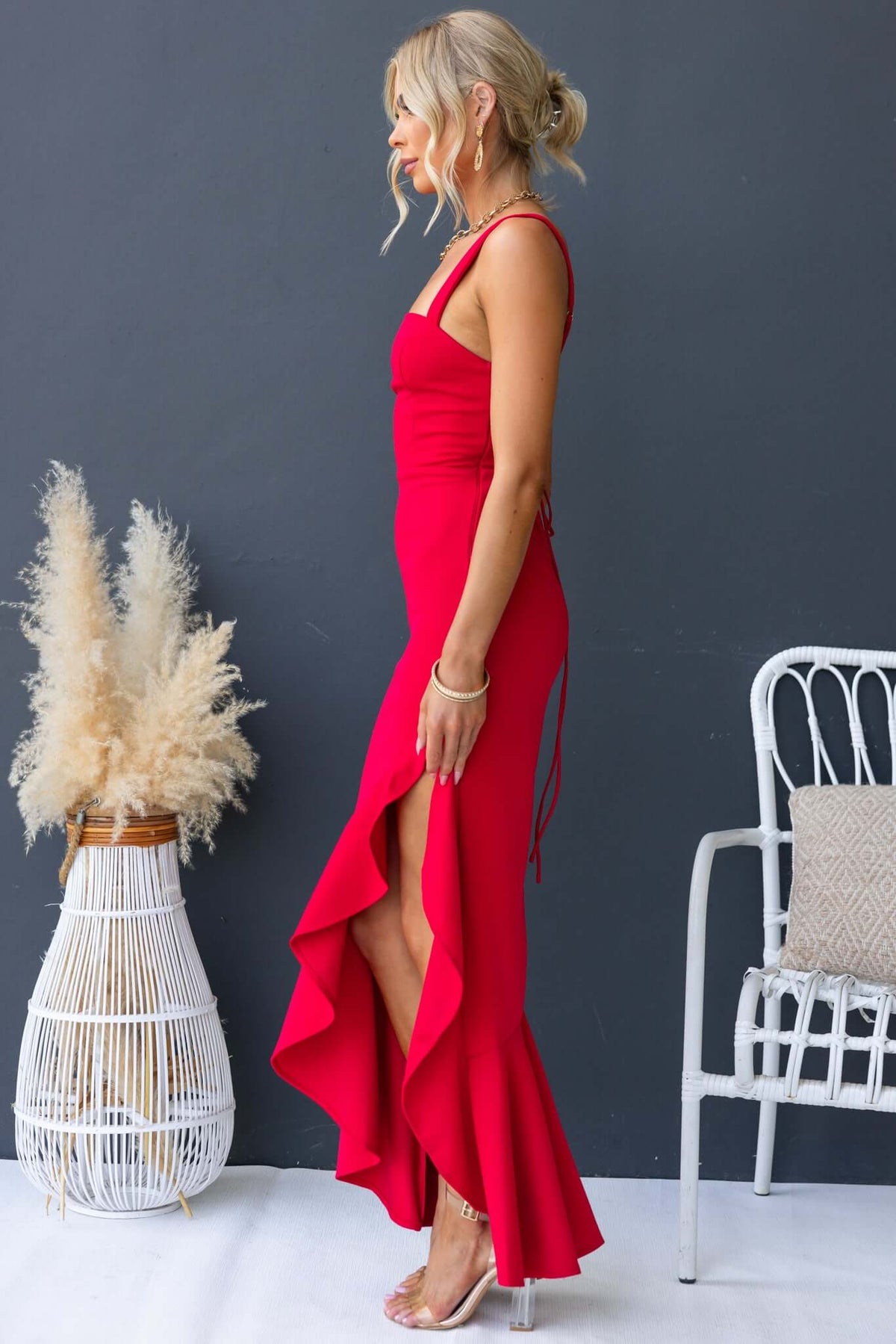 Acoma Maxi Dress in red with adjustable straps, side zip, and ruffled hem, worn by a model in a stylish setting.