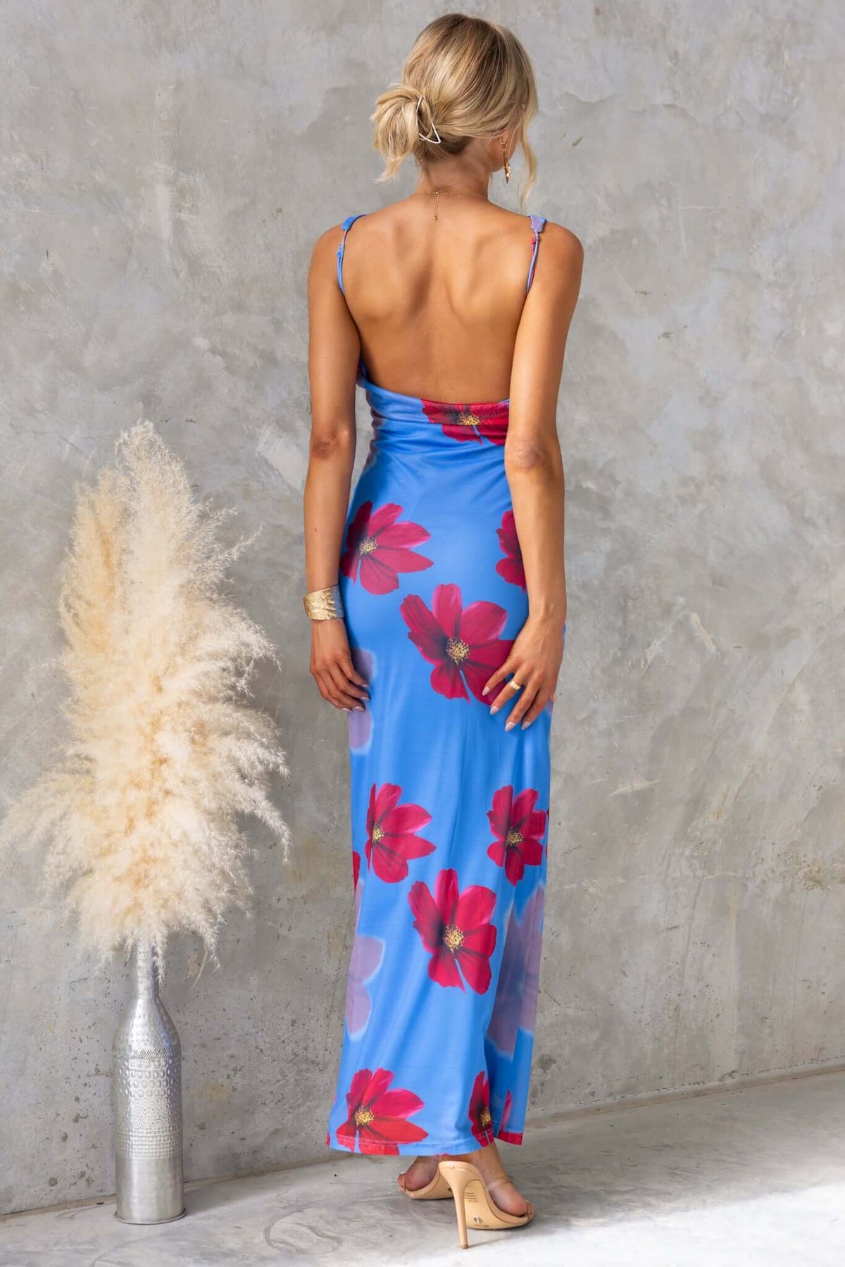 Back view of a woman in a blue Alvara maxi dress with floral print, showcasing adjustable straps and a low-cut back.
