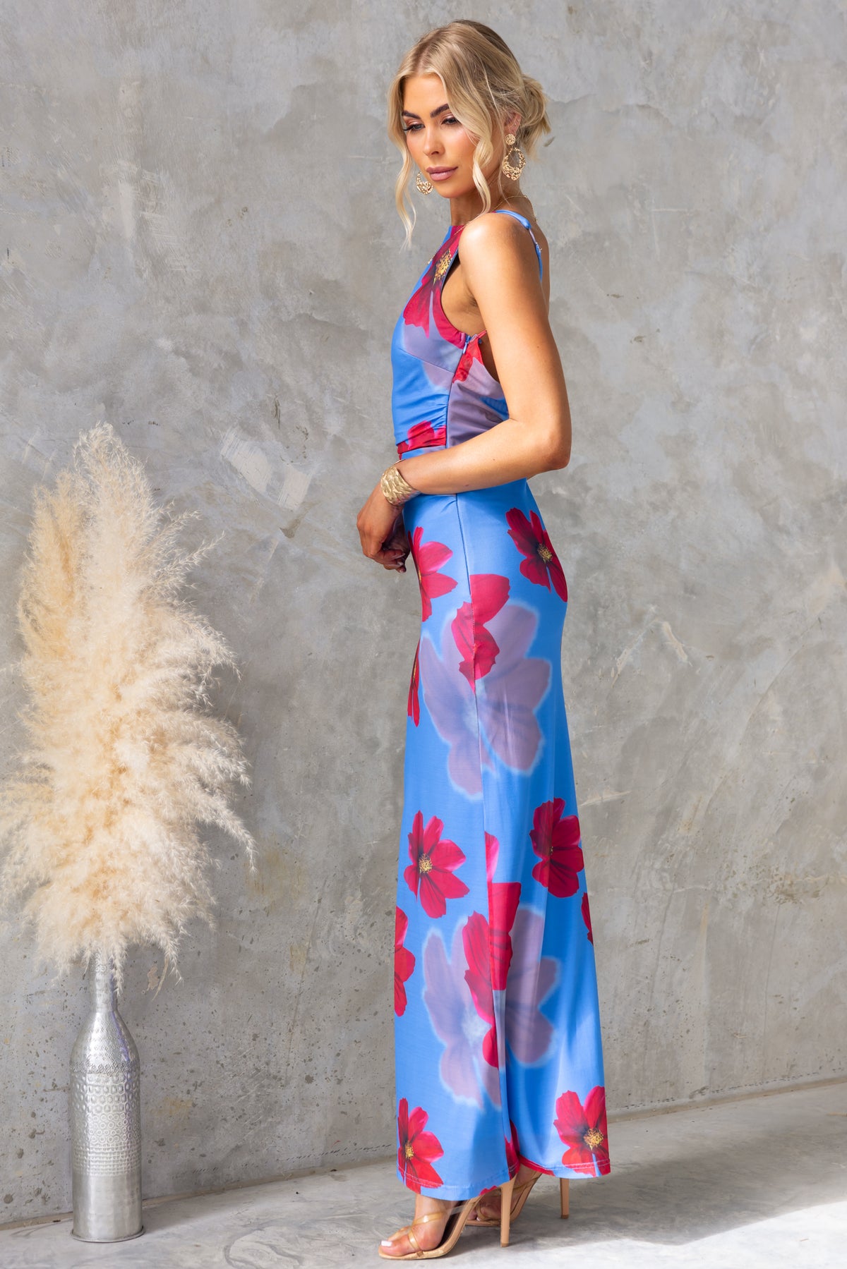 Model wearing Alvara Maxi Dress in blue with floral print, side view showcasing adjustable straps and low-cut back.