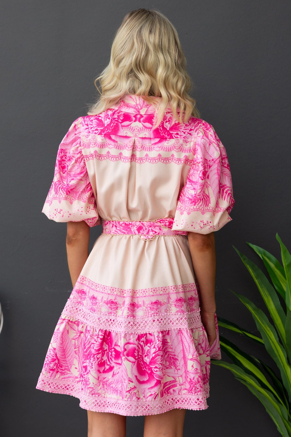 Back view of Cillie Dress featuring pink floral print, elastic sleeves, and a removable belt on a model.