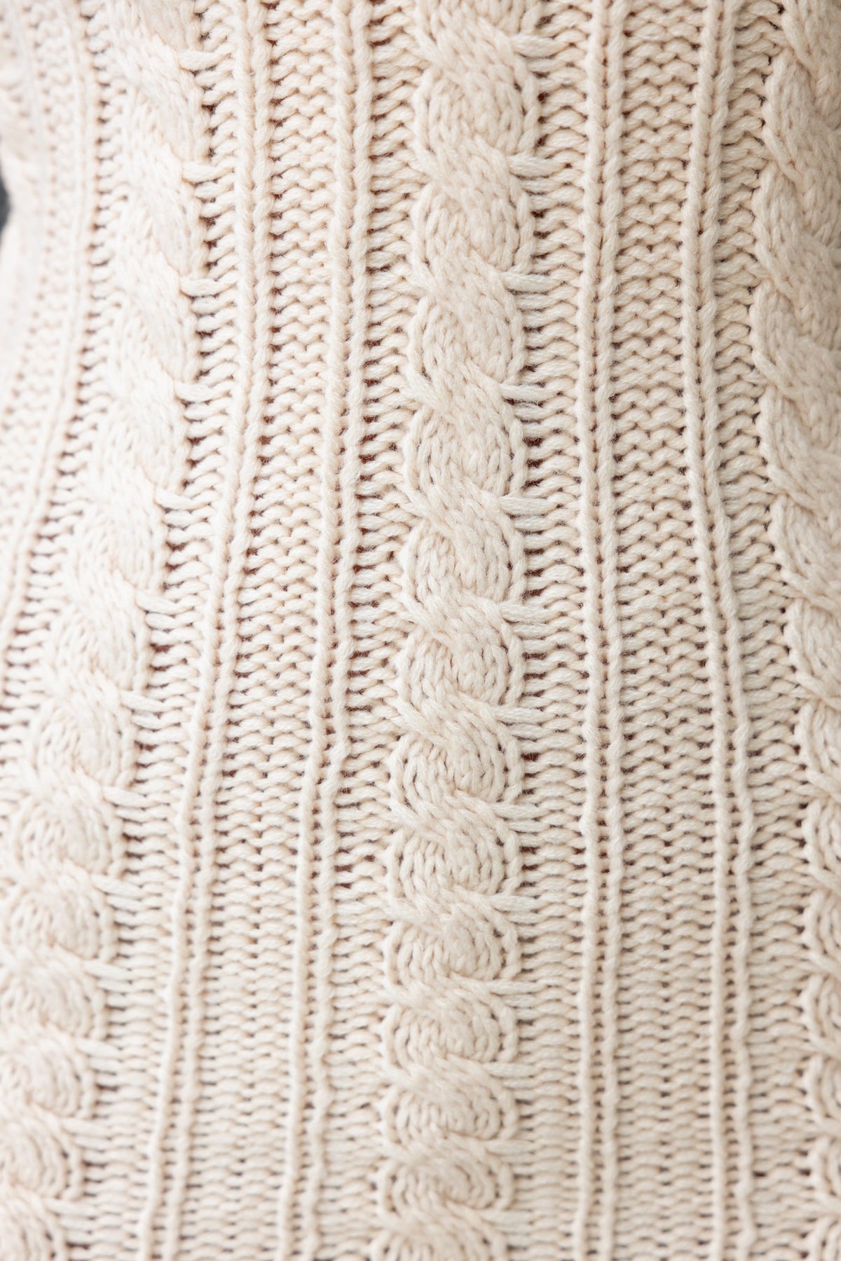 Close-up of textured cream knit fabric featuring cable stitch patterns.