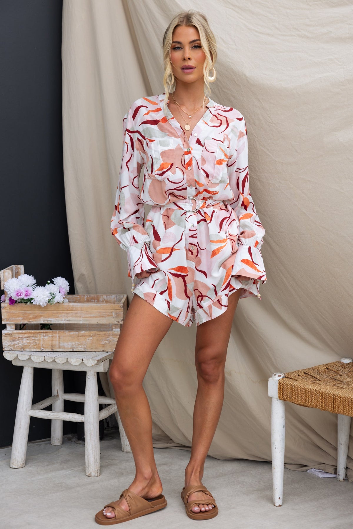 Woman wearing Alfred Playsuit featuring a floral pattern, button-up front, and pockets, styled with sandals.
