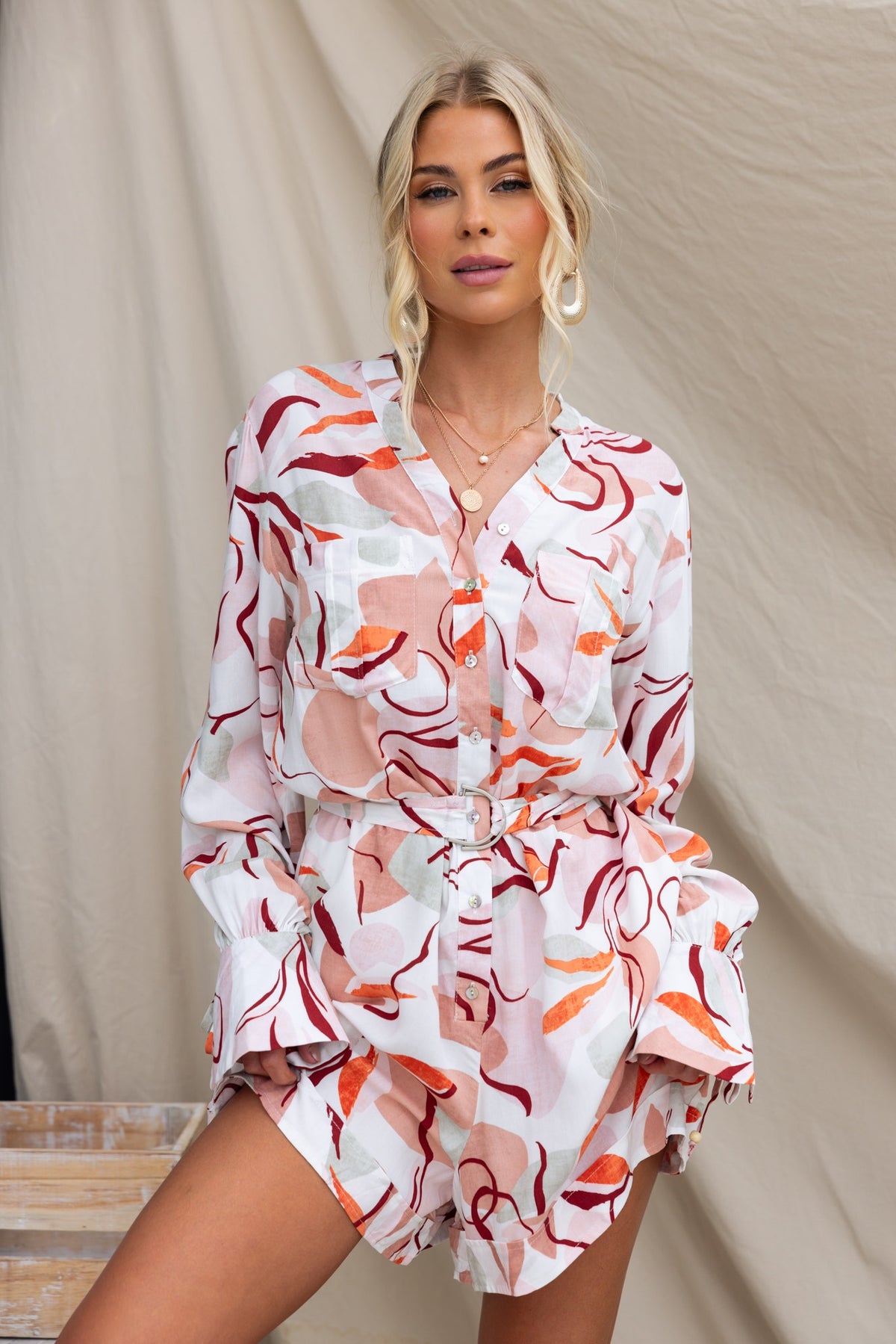 Woman wearing a stylish Alfred Playsuit with colorful patterns and a button-up front, featuring a removable belt.