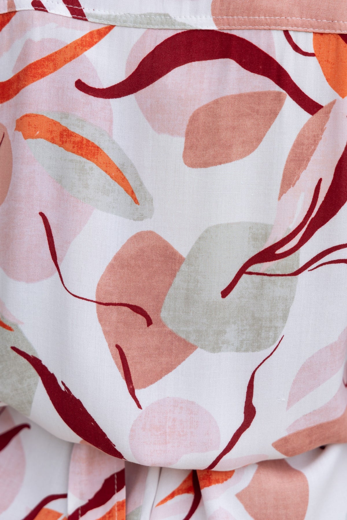 Close-up of abstract floral pattern in warm tones on Alfred Playsuit fabric, featuring soft textures and vibrant colors.