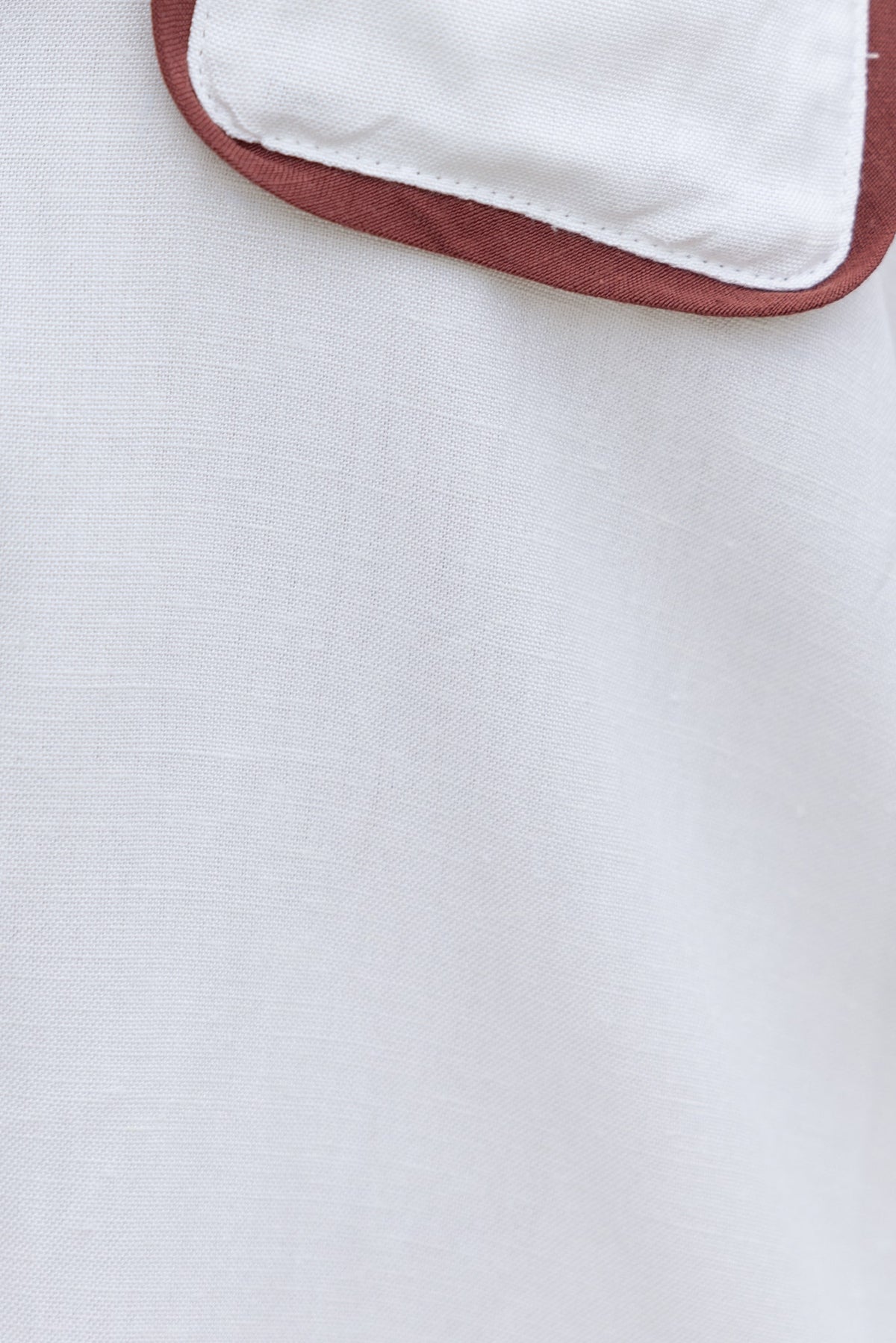 Close-up of the Ronnie Shirt featuring a white linen fabric and a rust-colored pocket detail.
