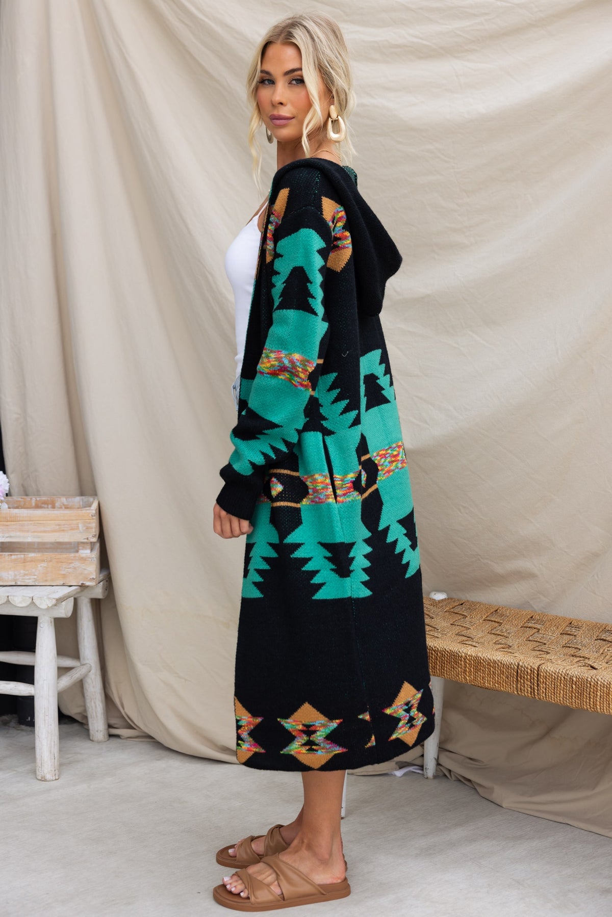 Model wearing a longline black cardigan with a vibrant green and ethnic print, styled with sandals.