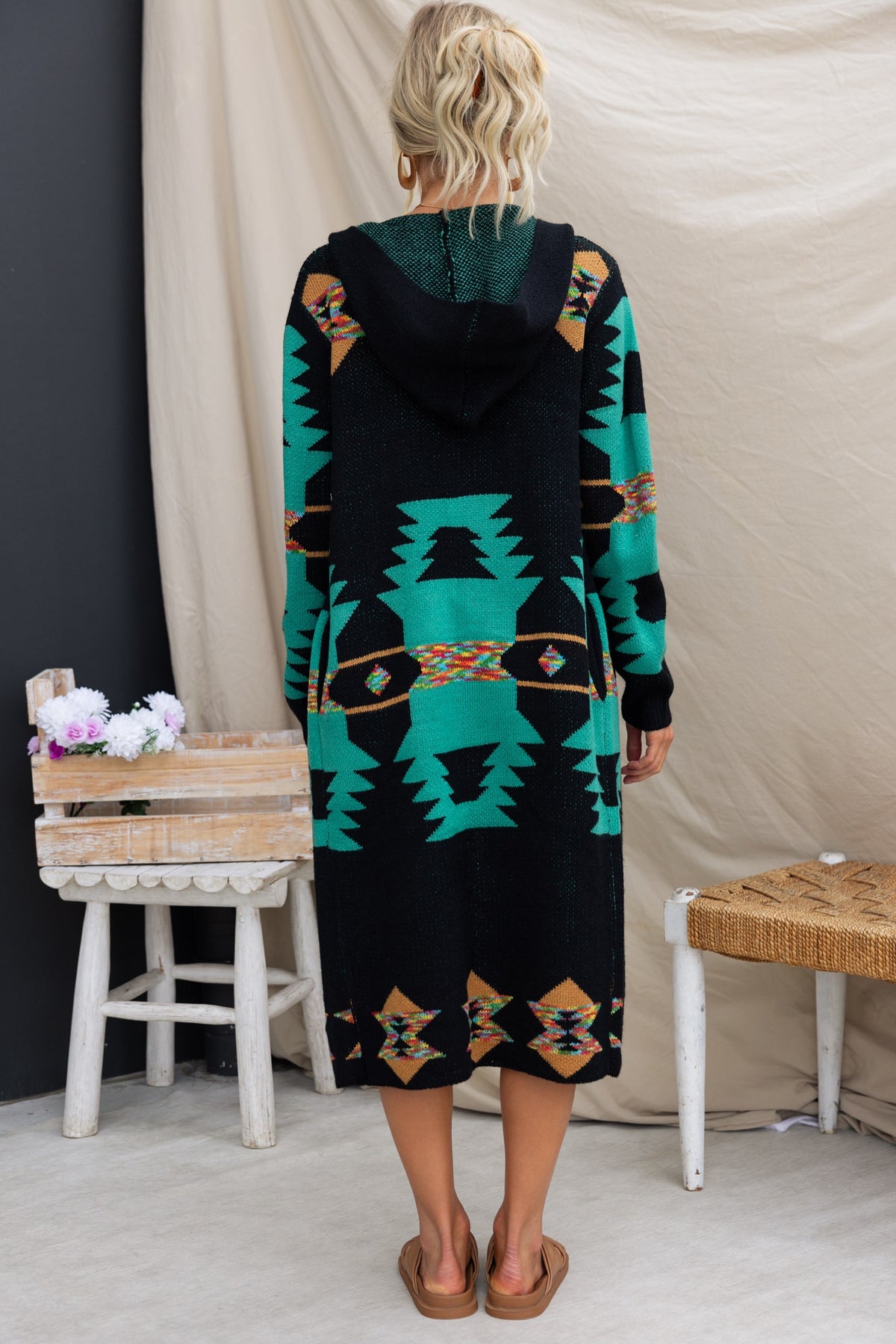 Back view of the Lazuli Cardigan, a longline black cardigan with turquoise patterns and a hood, ideal for casual wear.