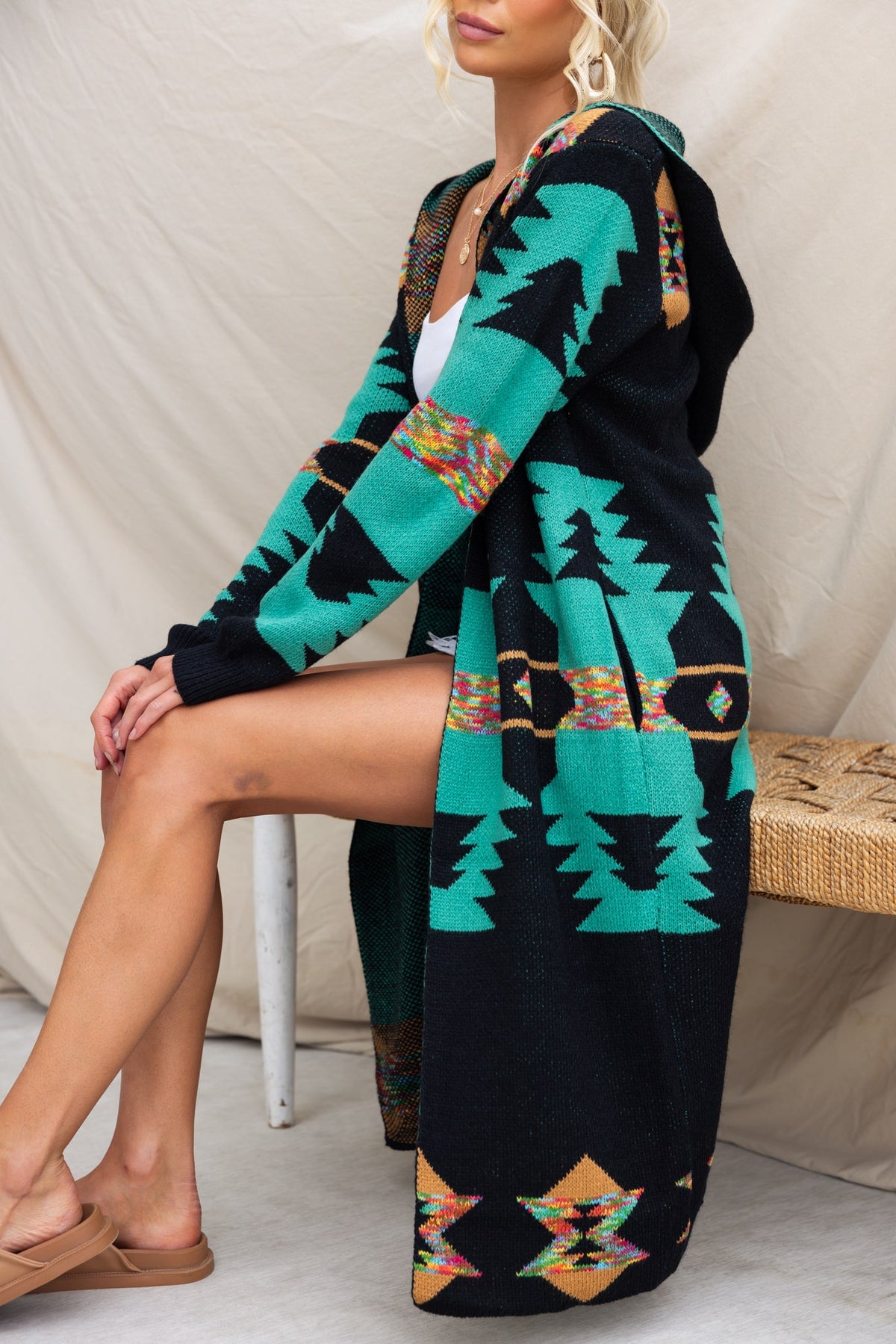 Longline black cardigan with colorful geometric patterns and hood, styled casually and featuring pockets.