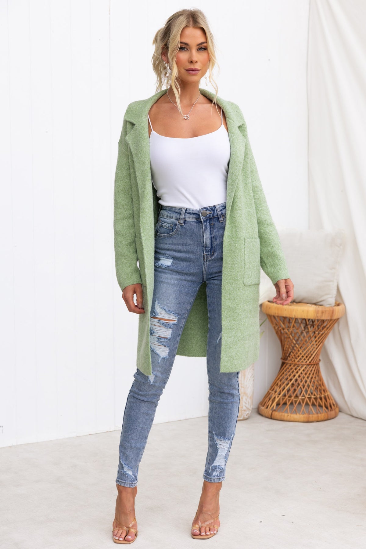Model wearing a green Sarlia Cardigan over a white tank top and distressed jeans, showcasing a stylish and cozy look.