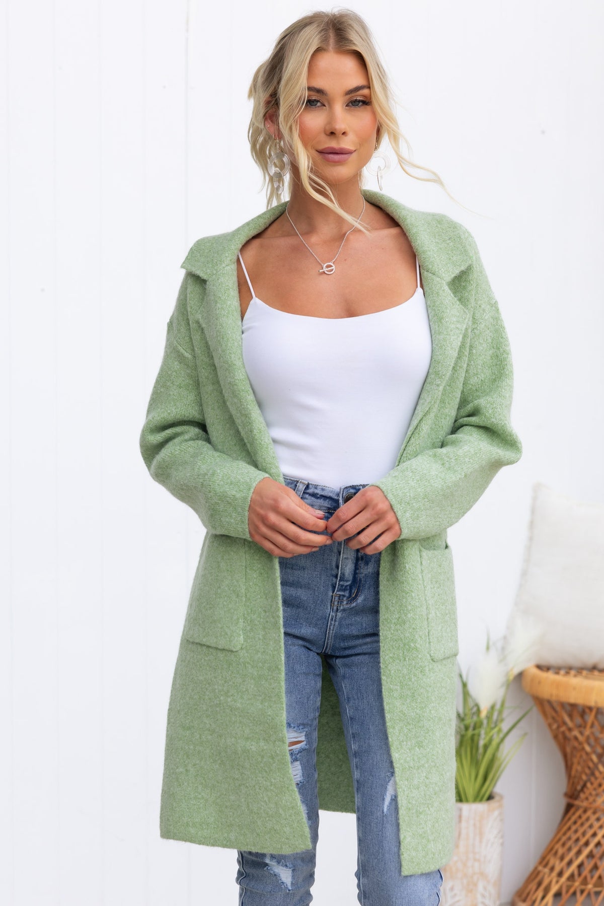 Woman wearing a light green Sarlia cardigan with pockets over a white tank top and distressed jeans.