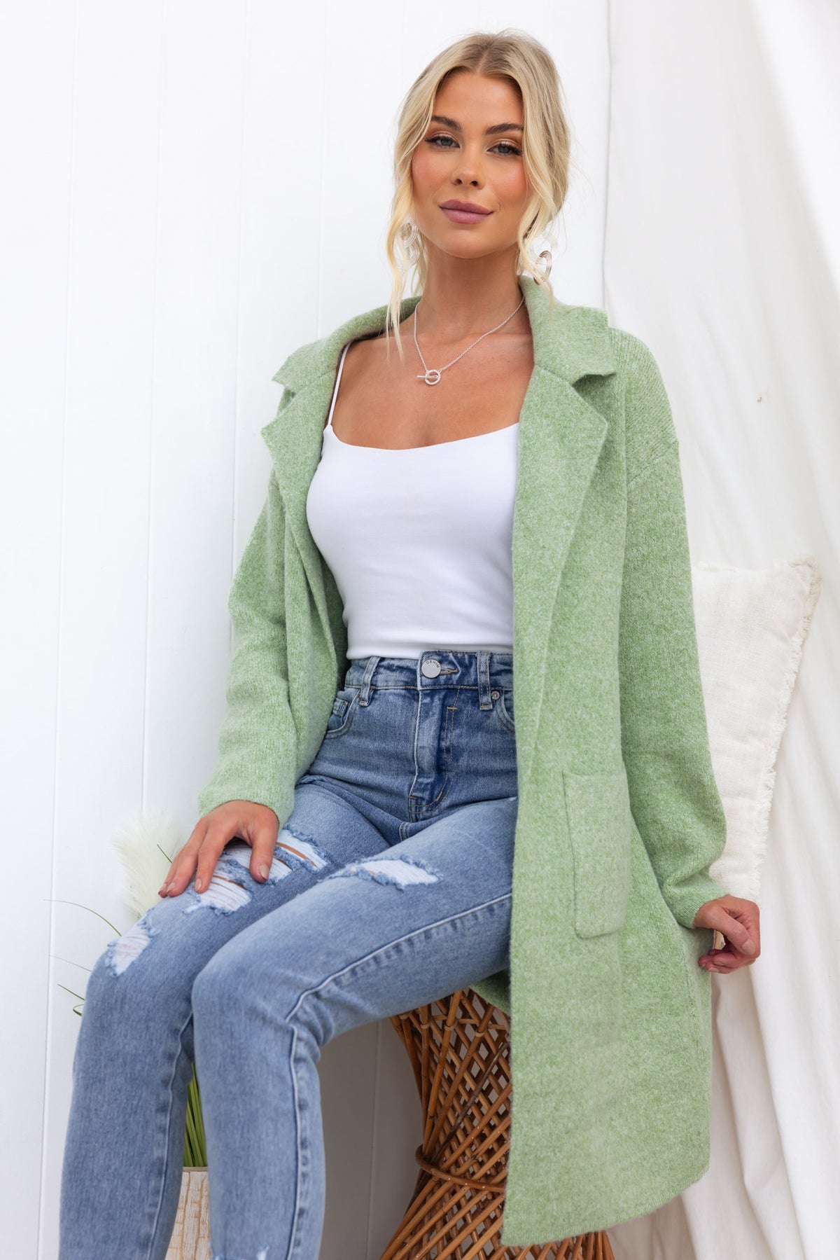 Sarlia Cardigan in soft green, worn over a white top and distressed jeans, featuring pockets and a relaxed fit.