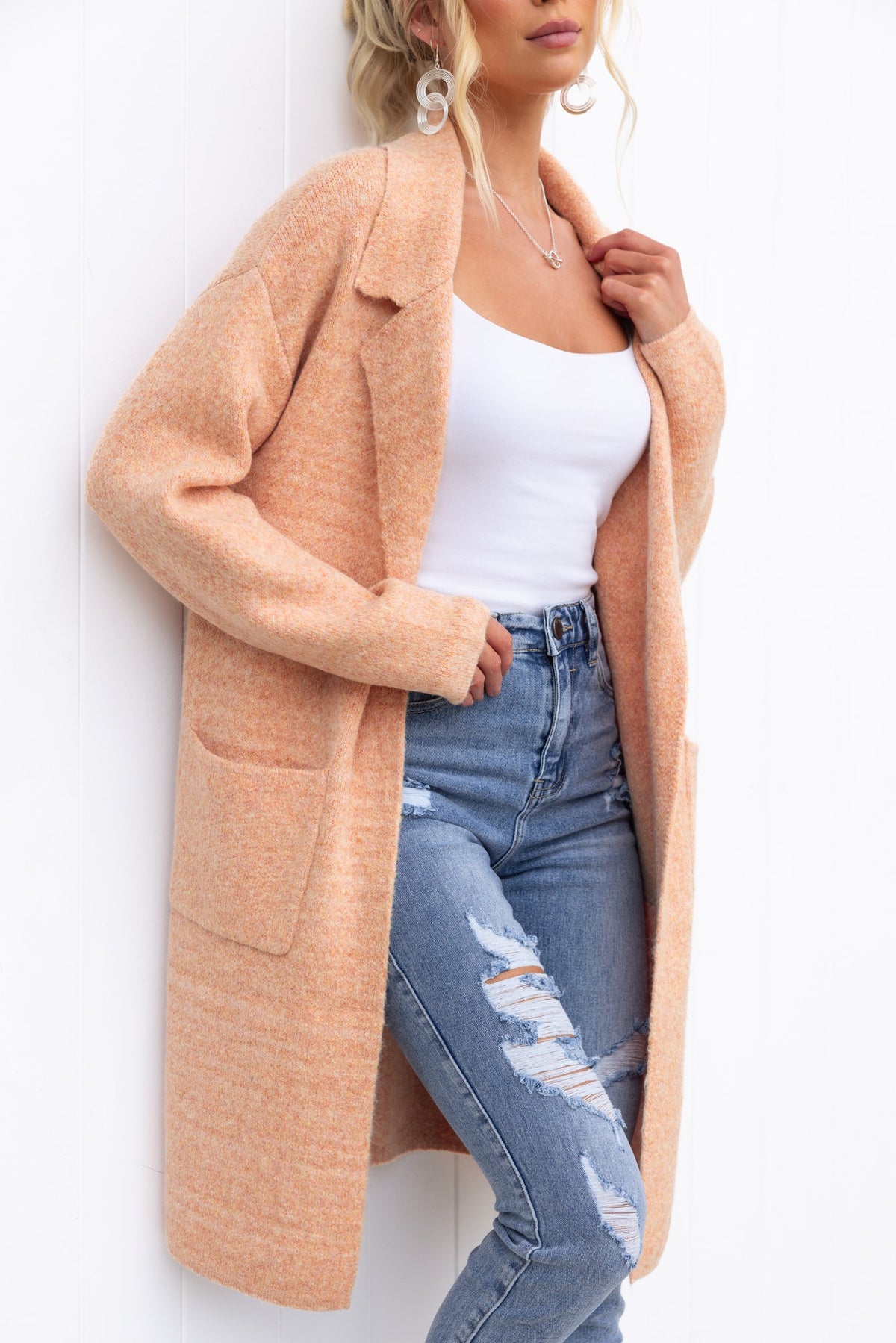 Sarlia Cardigan in soft peach hue, featuring a relaxed fit, front pockets, and worn with a white top and ripped jeans.