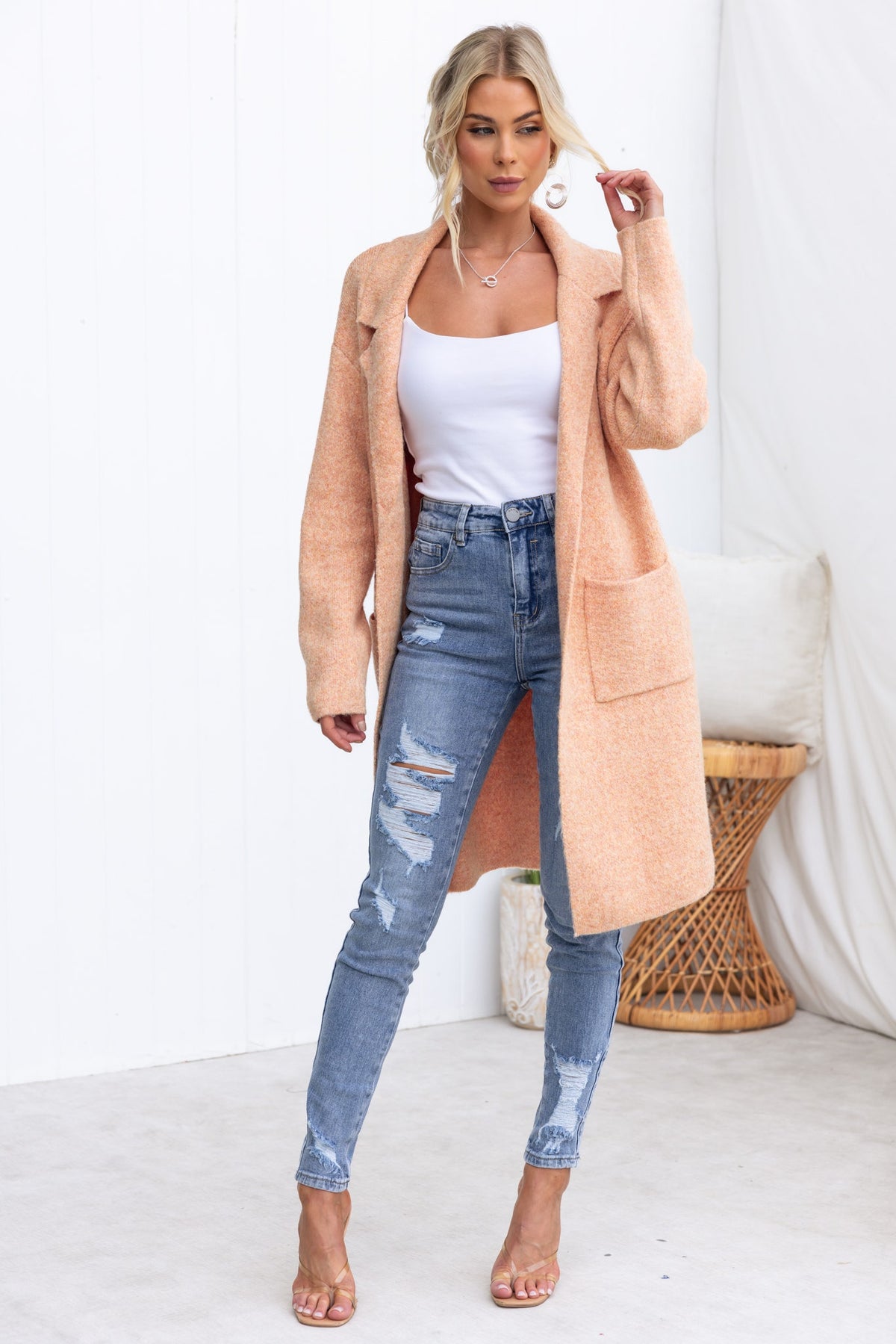 Stylish woman in a Sarlia cardigan, white top, and ripped jeans, showcasing a relaxed fit and knit design.