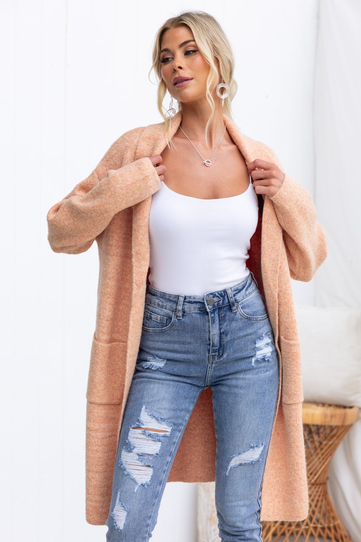 Model wearing a Sarlia cardigan with pockets over a white tank top and ripped jeans, showcasing its relaxed fit and knit material.