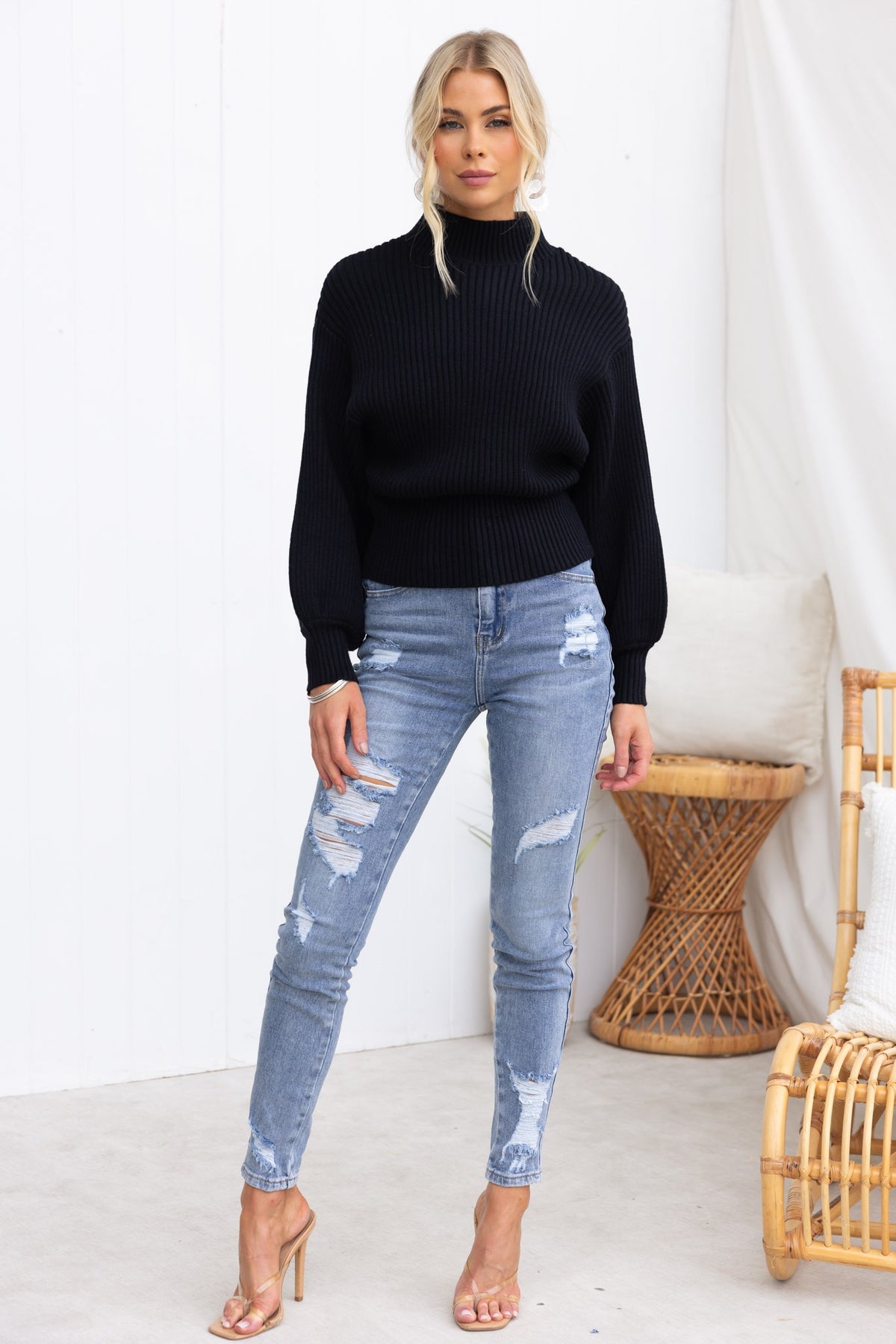 Sola Jumper in black, featuring mock neckline and wide sleeves, paired with distressed blue jeans on model in stylish setting.