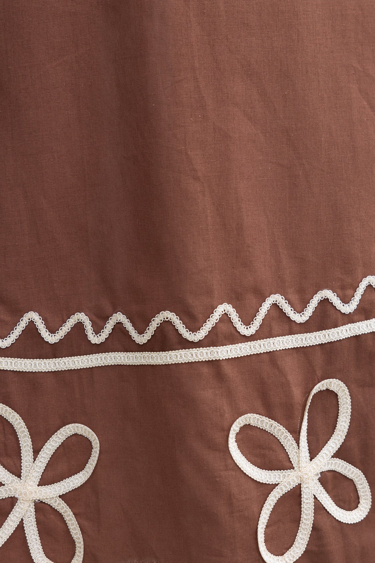 Close-up of brown fabric featuring white embroidered flowers and decorative stitching for Azurra Maxi Dress.