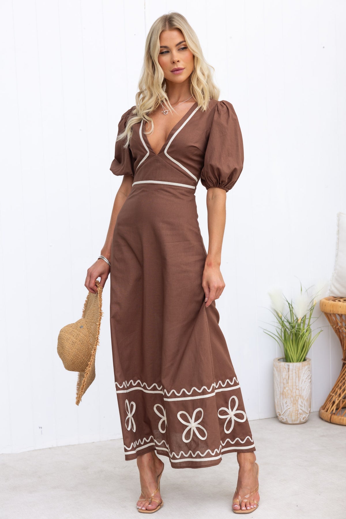 Azurra Maxi Dress in brown with puff sleeves and floral embroidery, perfect for summer outings. Model accessorized with a straw hat.