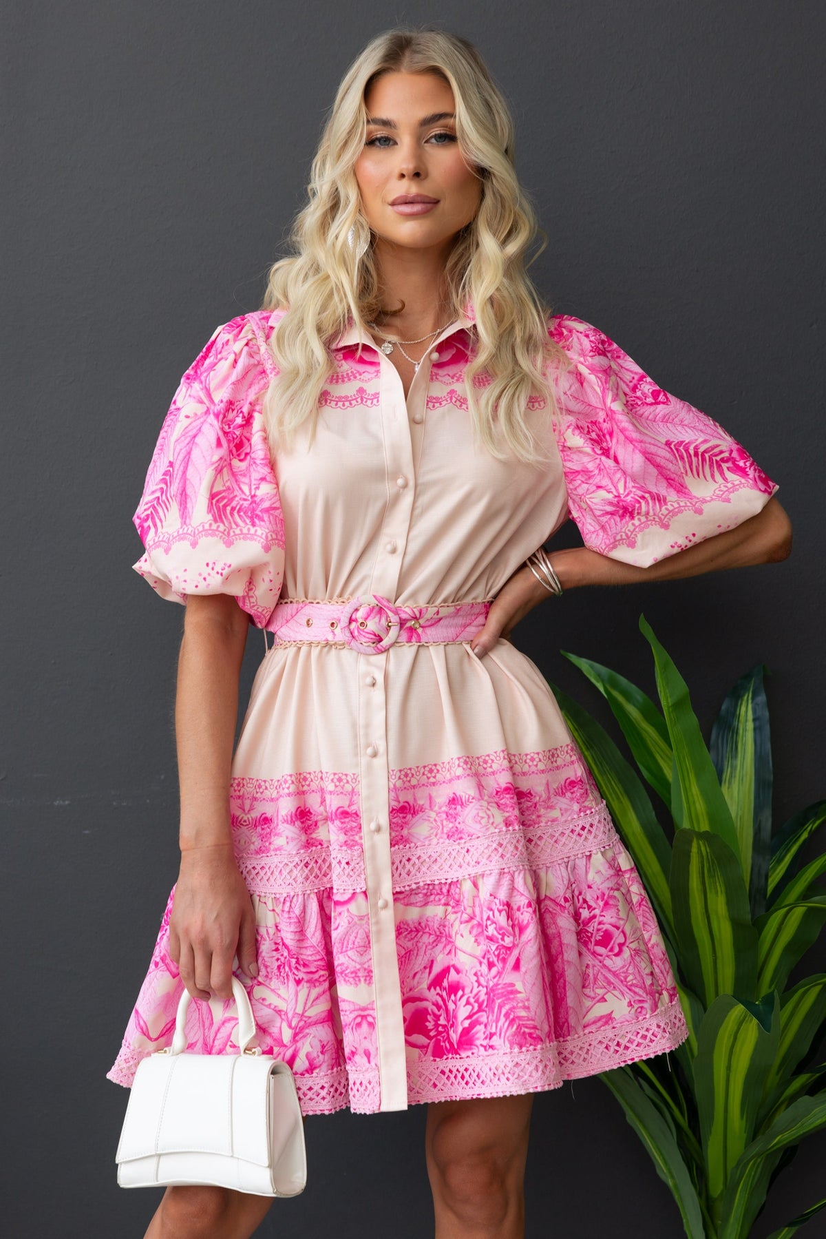 Model wearing Cillie Dress, a floral print button-up dress with puff sleeves and removable belt, styled with a white handbag.