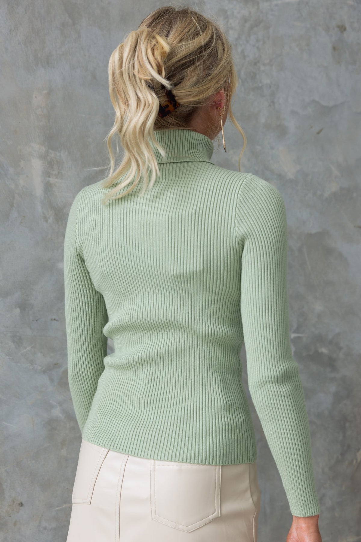 Back view of woman wearing a mint green ribbed knit Narla Top with turtle neckline and long sleeves.