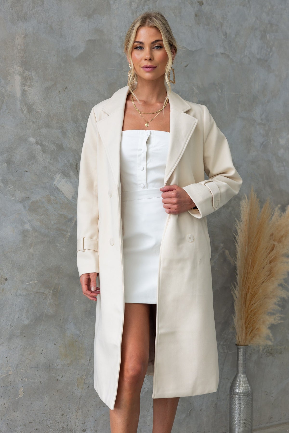 Model in a longline cream Lansen coat with collar and lapel, styled over a white dress.