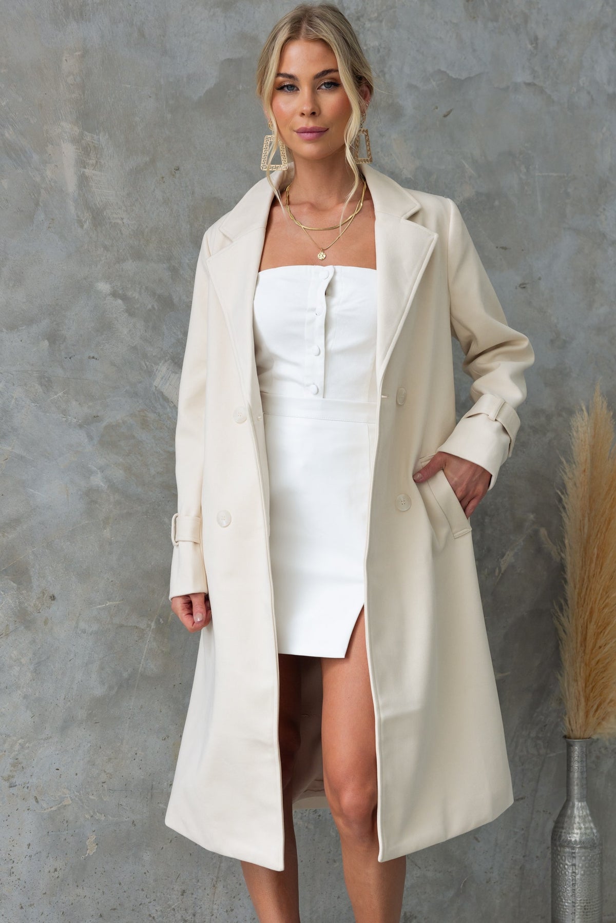 Model wearing Lansen Coat in cream, featuring a longline fit, collar, and button-up front against a textured backdrop.