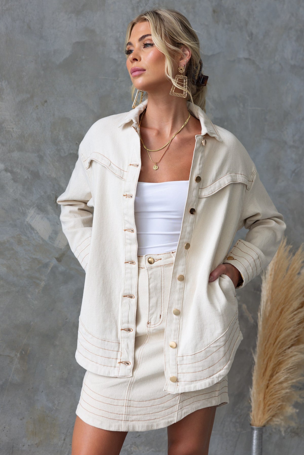 Model wearing a cream denim shacket with button-up front and pockets, styled with a white top and matching skirt.