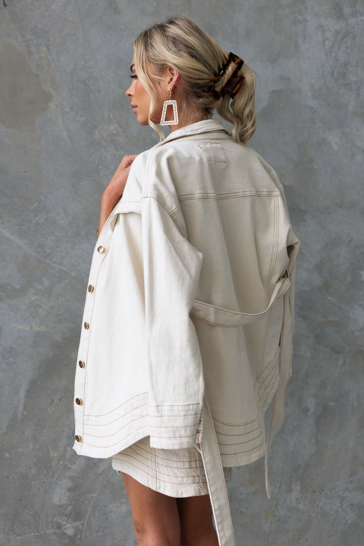 Model showcasing a cream-colored denim shacket featuring a collar, button-up front, and removable tie.