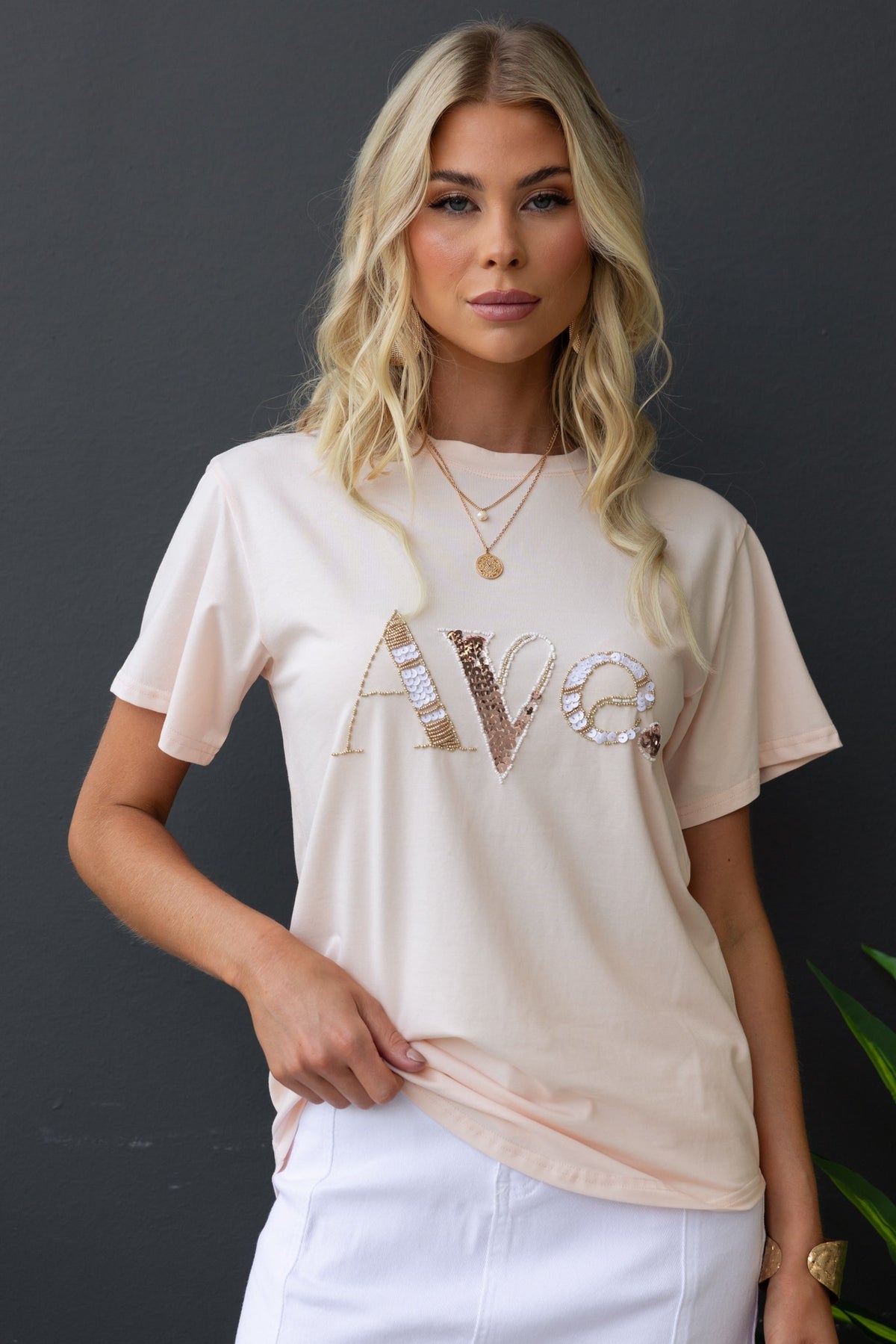 Model wearing a soft pink Cesca Tee with 'Ave' bead detail, showcasing a casual and stylish round neckline.