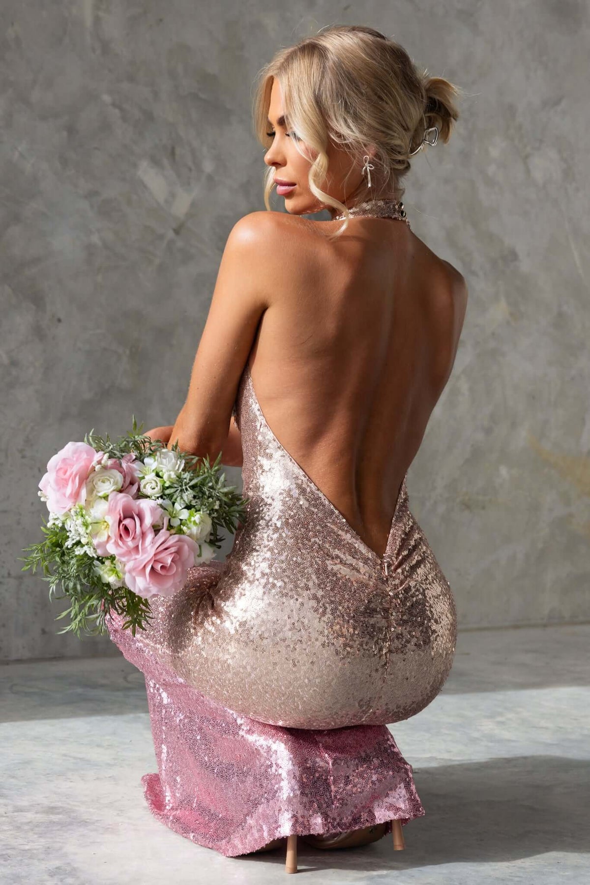 Model showcasing Amaris Maxi Dress with a cowl neckline and sequins, holding a bouquet of flowers from behind.