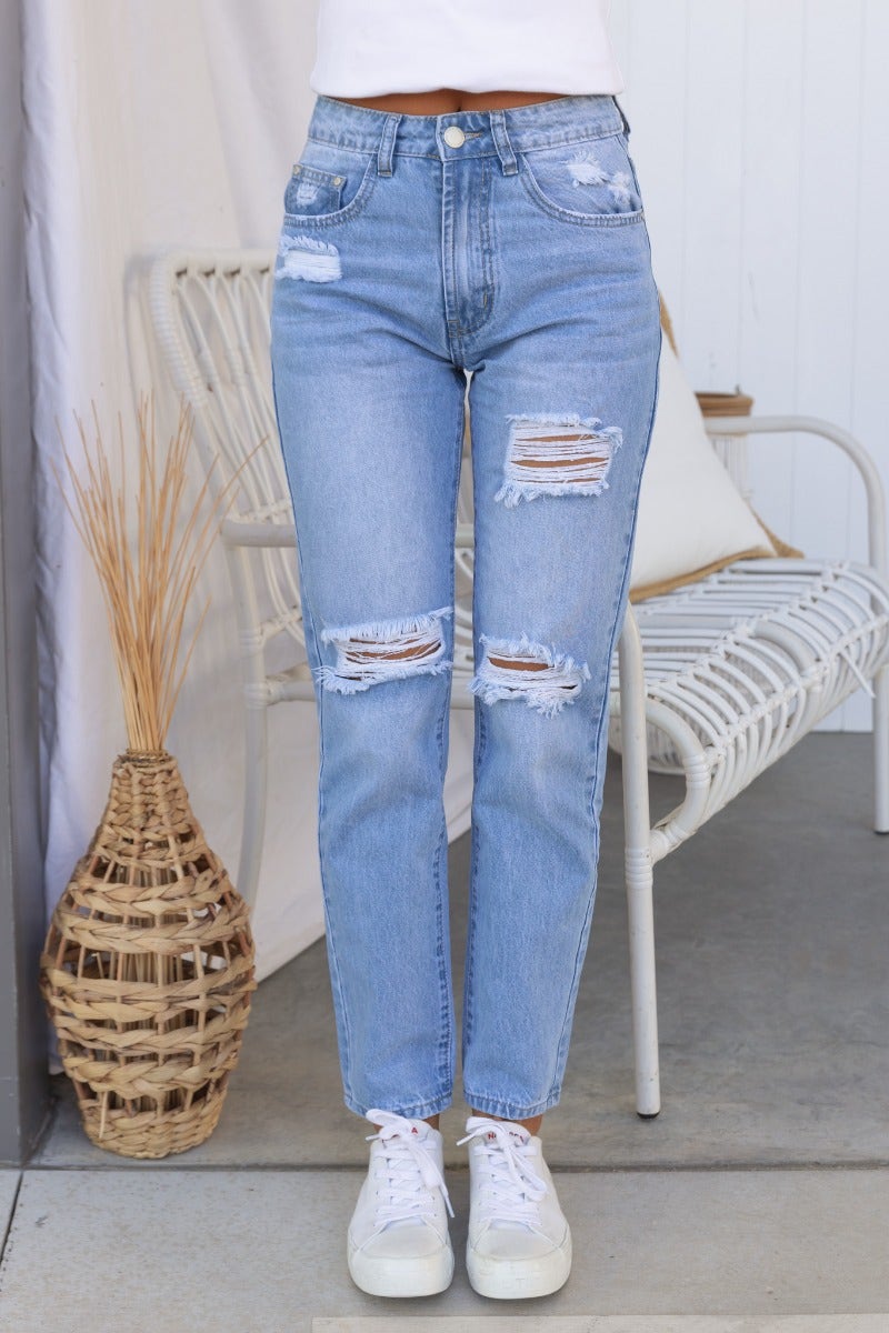 Light blue distressed denim jeans with rips at the front, styled with a mid-high waist and straight leg fit.