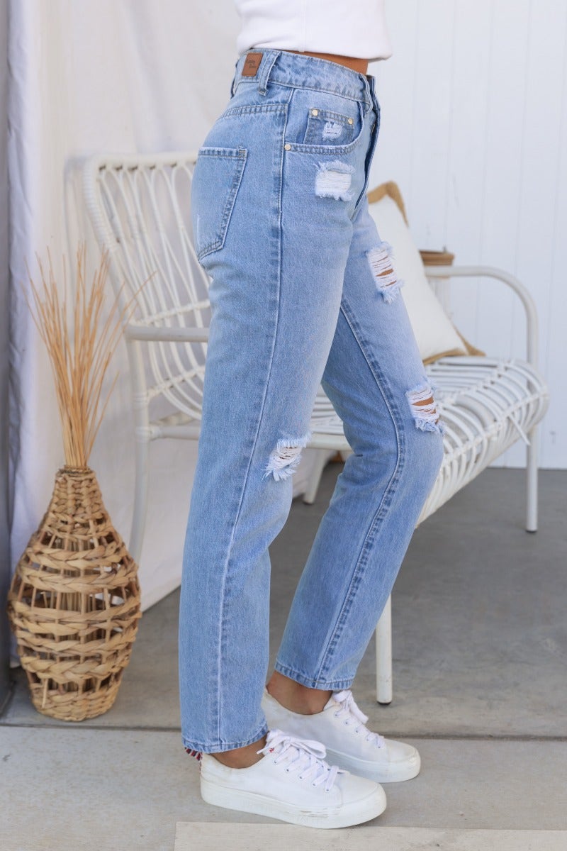 Model wearing All The Time distressed denim jeans in blue with rips, featuring mid-high waist and straight leg fit.