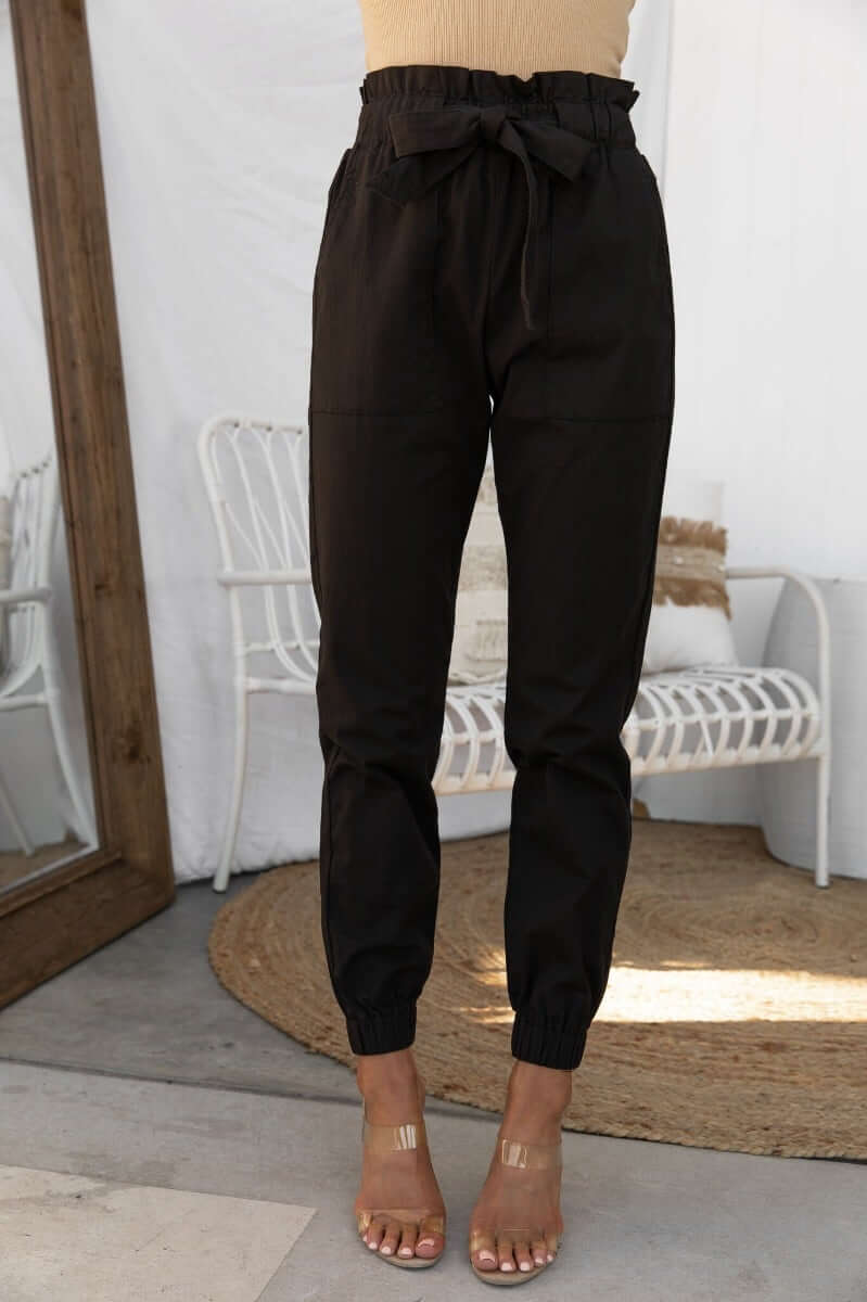 Black Zol Pants with elastic waistband, removable fabric belt, and pockets, styled on model.