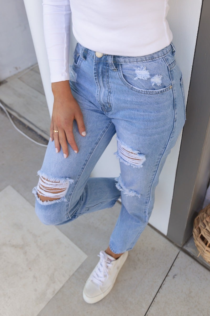 Woman wearing All The Time distressed jeans, mid-high waist with rips, paired with white sneakers.