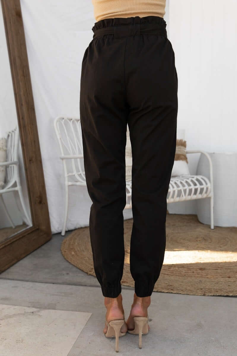 Zol Pants in black with elastic waistband and cuffs, styled with a removable belt, showing the back view.