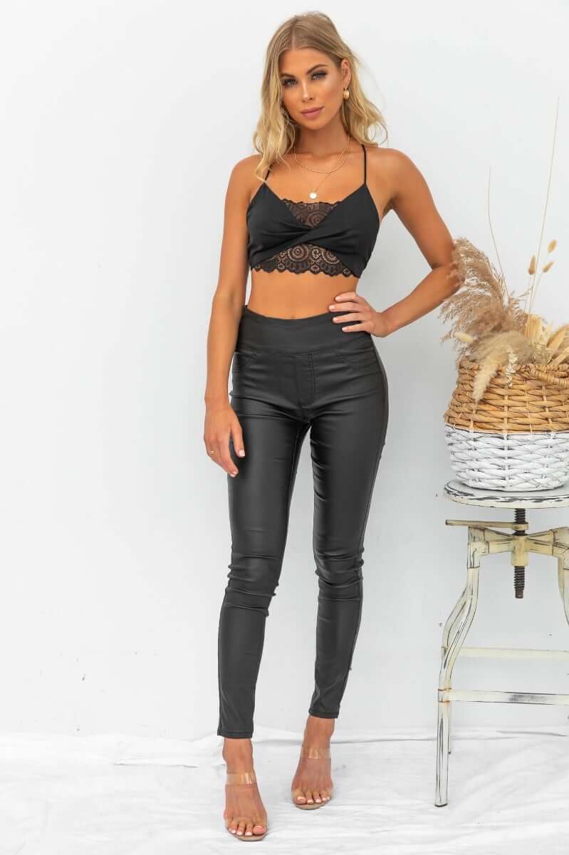 Model wearing Damar Pants, wet look black faux leather with firm stretch, styled with a black lace crop top.